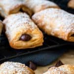 image with text. text reads "3 ingredients chocolate pastry puffs". image is crispy puff pastry rolls cut in half showing with chocolate in the centre, more in the background.