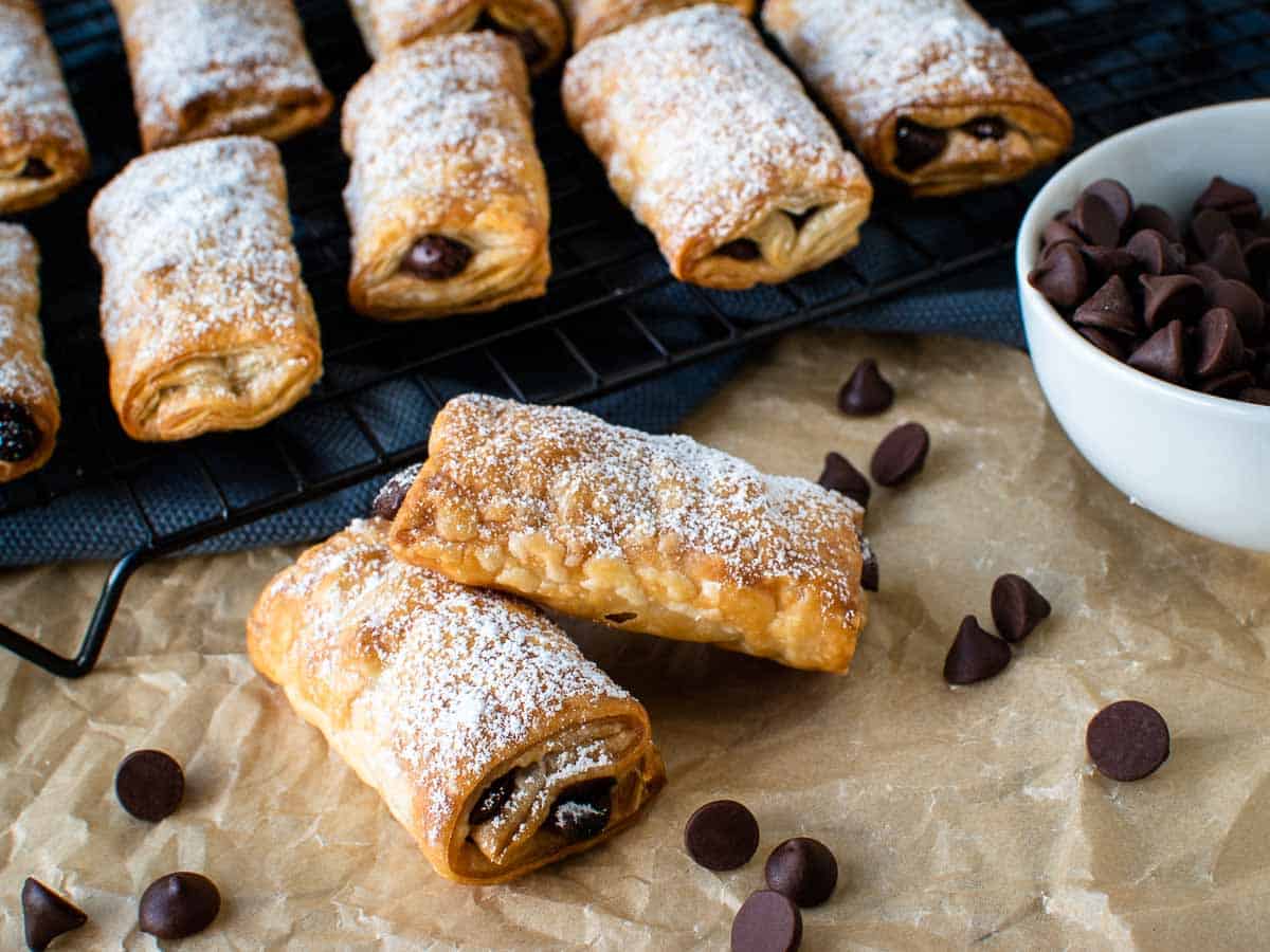 Chocolate filled puff pastries dusted with powdered sugar with chocolate chips scattered and some in a bowl.