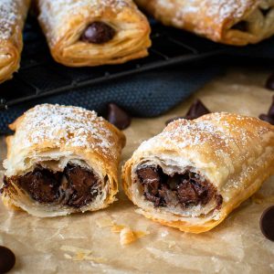 crispy puff pastry rolls cut in half showing with chocolate in the centre, more in the background.