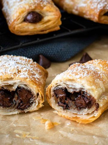 crispy puff pastry rolls cut in half showing with chocolate in the centre, more in the background.