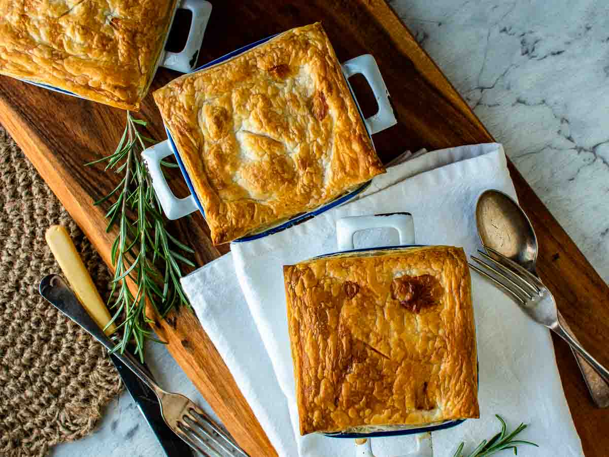 Three pastry topped pies on wooden board viewed from above.