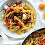 Twirly pasta salad on white plate with large bowl of pasta on the side.
