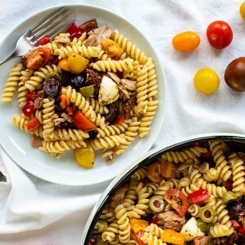 Twirly pasta salad on white plate with large bowl of pasta on the side.