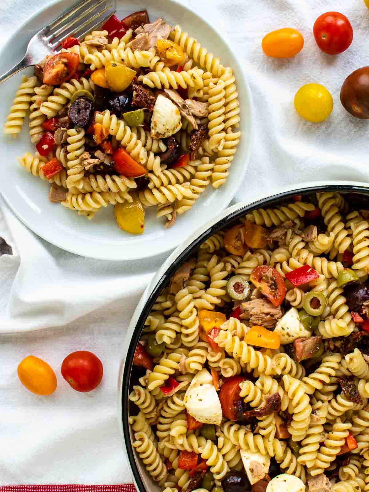 The zesty Italian pasta salad on white plate with large bowl of pasta on the side.