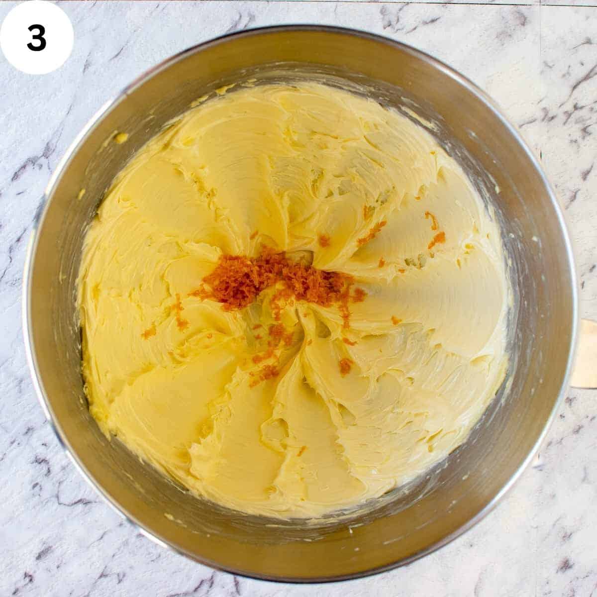 Creamed butter and sugar in a bowl with orange zest on top.