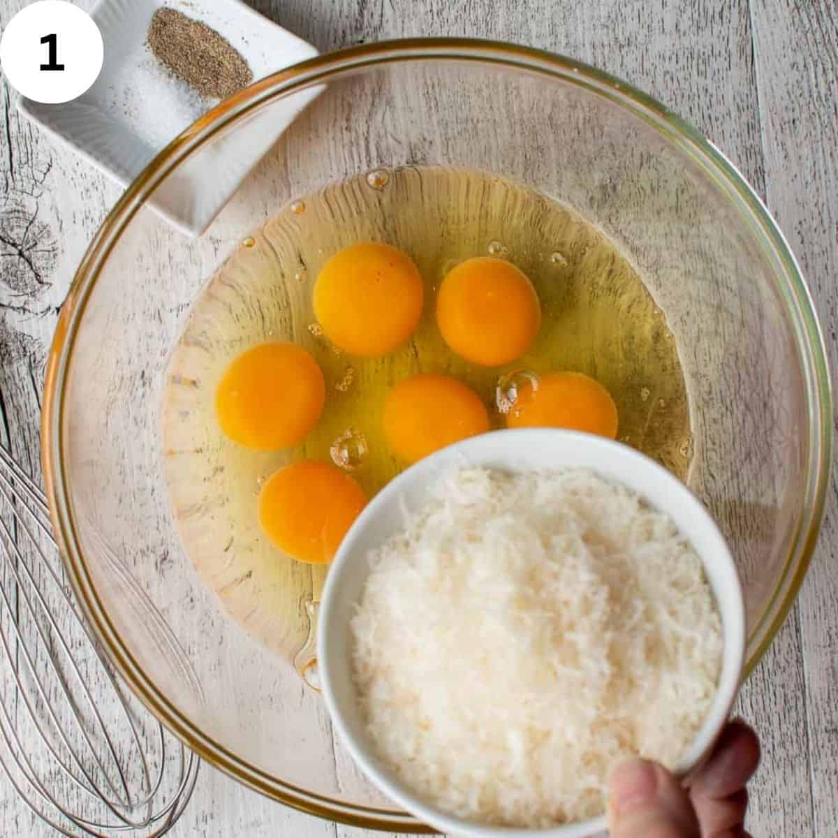 Grated parmesan cheese being added to eggs in a bowl.