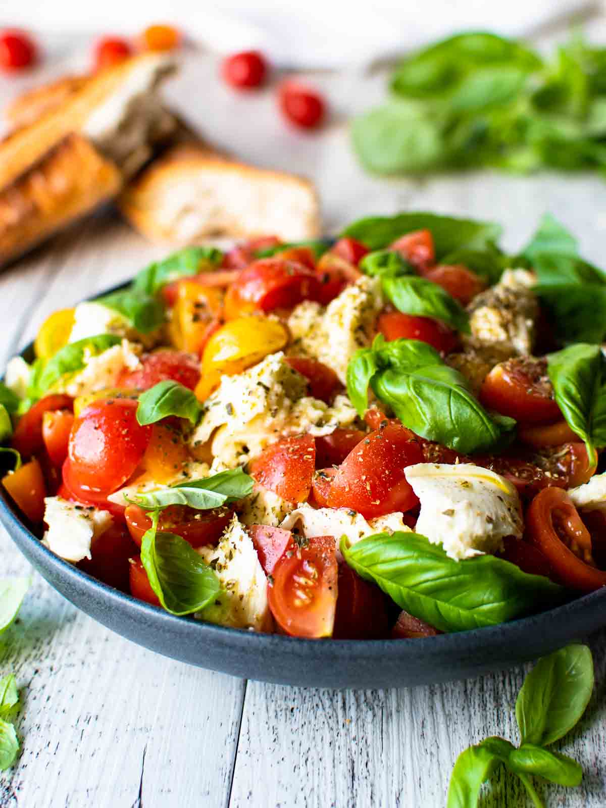 Shallow bowl of cherry tomato Caprese salad with garlic bread in the background. 