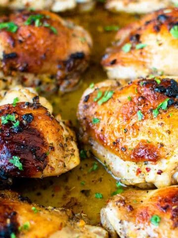 Baked Italian chicken thighs in baking pan garnished with parsley.