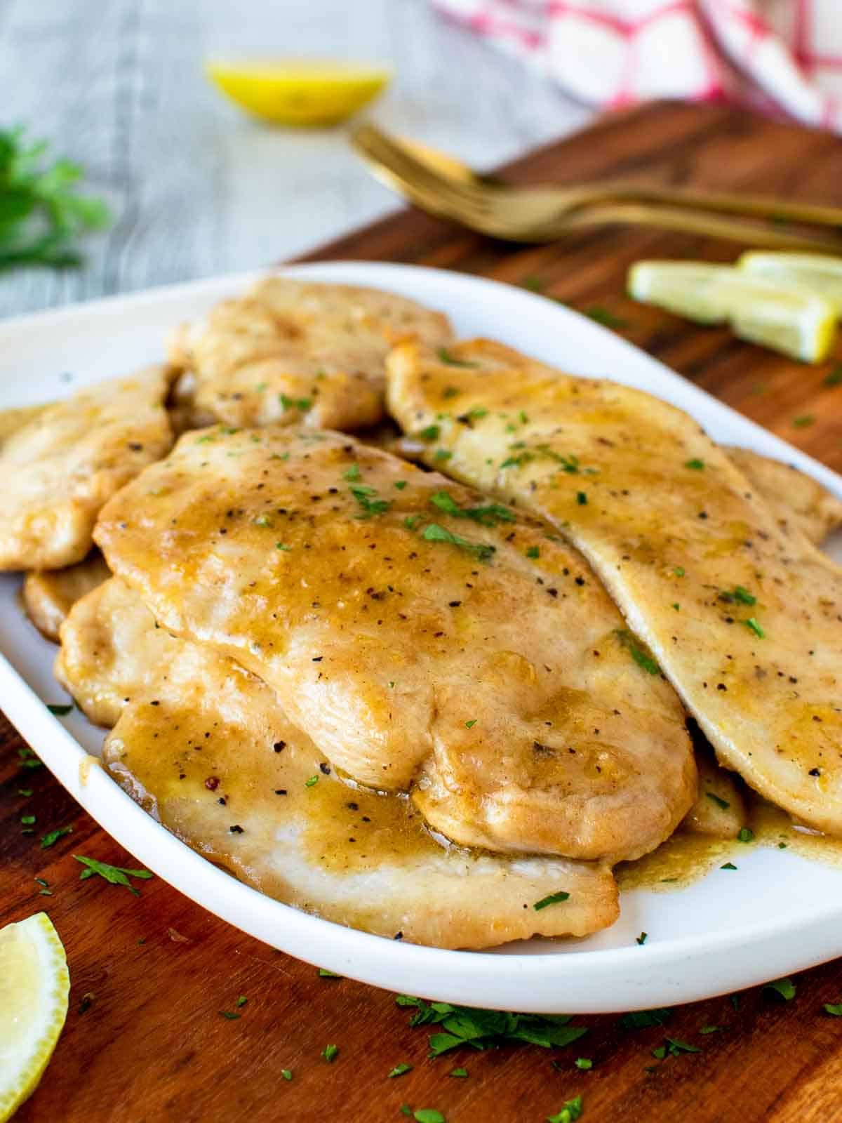 Chicken Limone cutlets on a white plate garnished with chopped parsley.