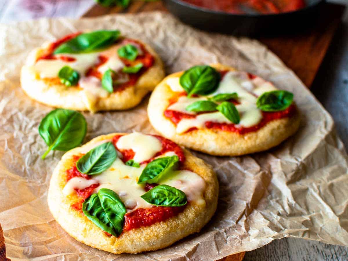 Three pizzas in a staggered row with tomato sauce, cheese and basil leaves on top.