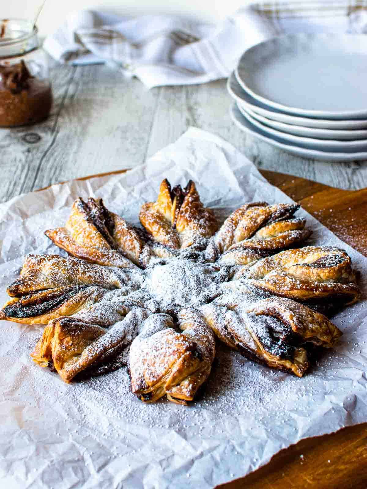 Puff pastry with Nutella on white paper dusted with powdered sugar.