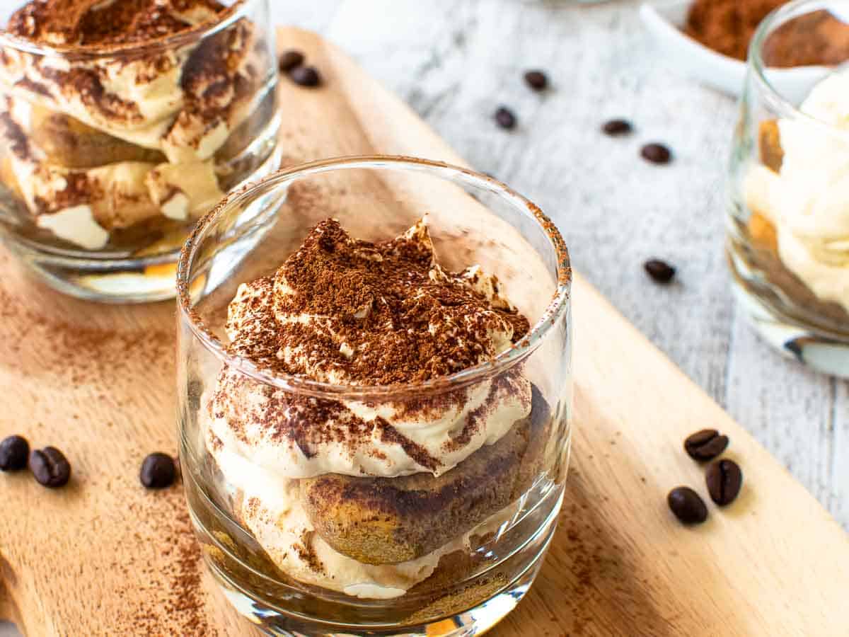 Clear glasses with layered creamy dessert on wooden board.