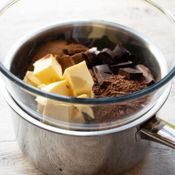 Butter, cocoa powder and chocolate in glass bowl in a steel saucepan.
