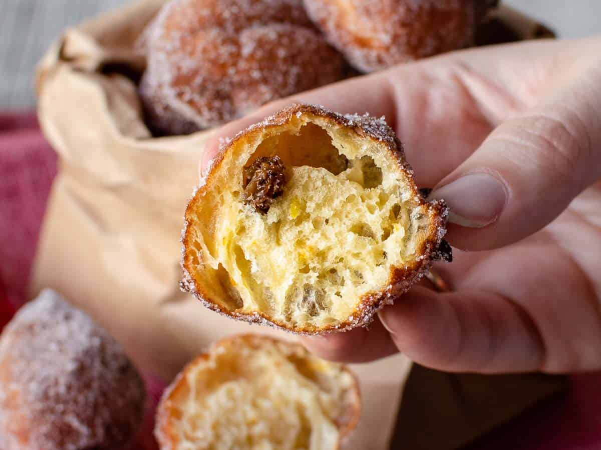 Close up of theThese Frittelle are the perfect combination of crispy on the outside and chewy on the inside.  inside of a fried dough ball held by fingers.