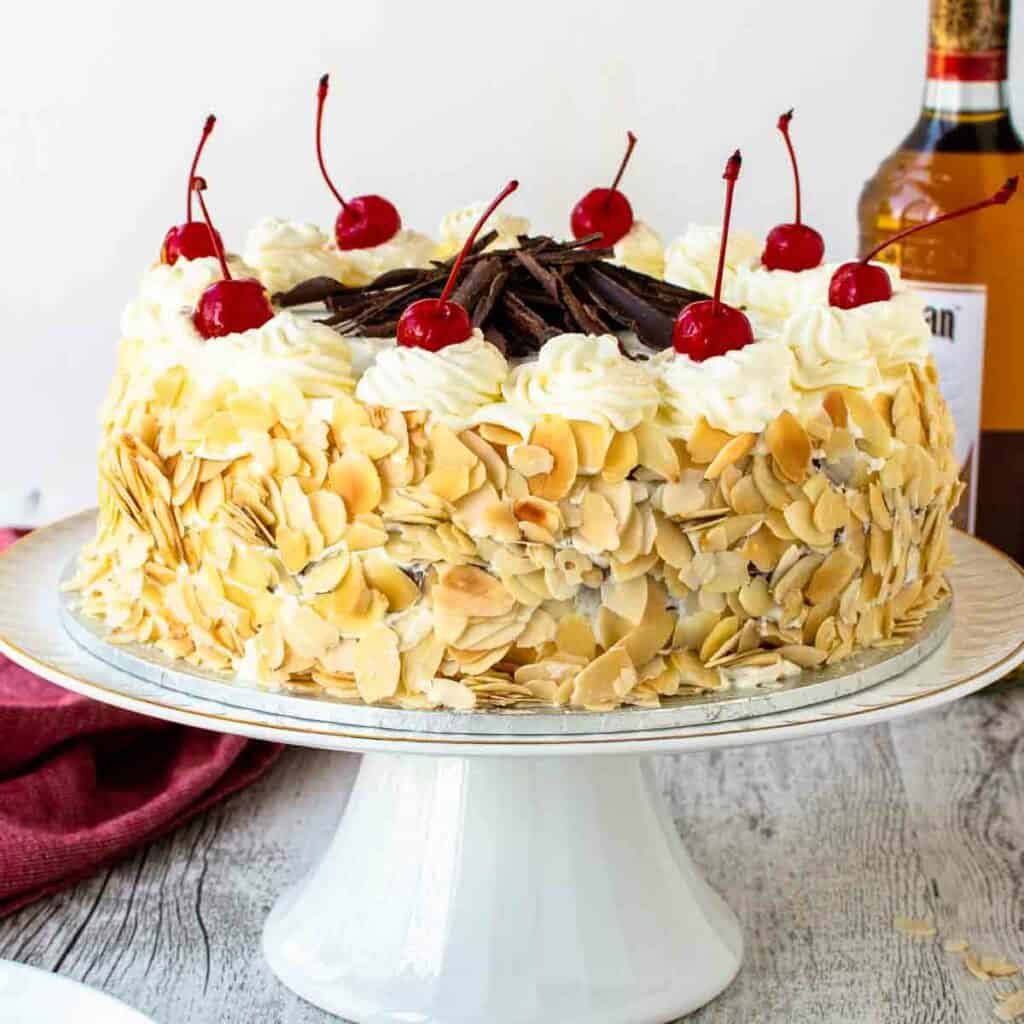 Italian rum cake on a white cake stand topped with maraschino cherries.