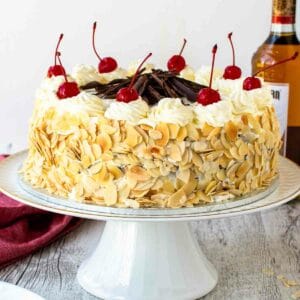 Italian rum cake on a white cake stand topped with maraschino cherries.