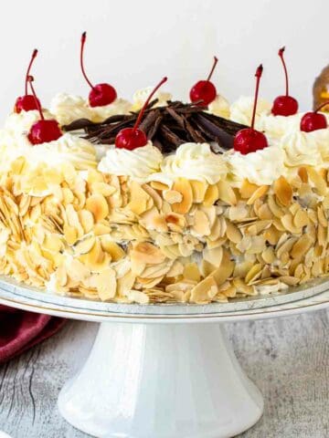 Italian rum cake on a white cake stand topped with maraschino cherries.