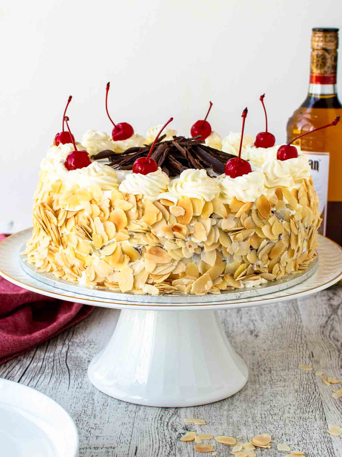 Italian rum cake on a white cake stand topped with maraschino cherries.