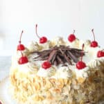 Italian rum cake on a white cake stand topped with maraschino cherries.