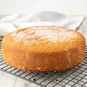 Pan Di Spagna on a black wire rack with granulated sugar on top.