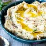 Mashed potatoes with red skin in a blue bowl with melted butter on top.