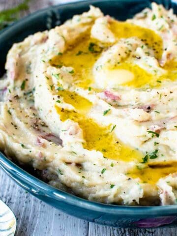 Mashed potatoes with red skin in a blue bowl with melted butter on top.