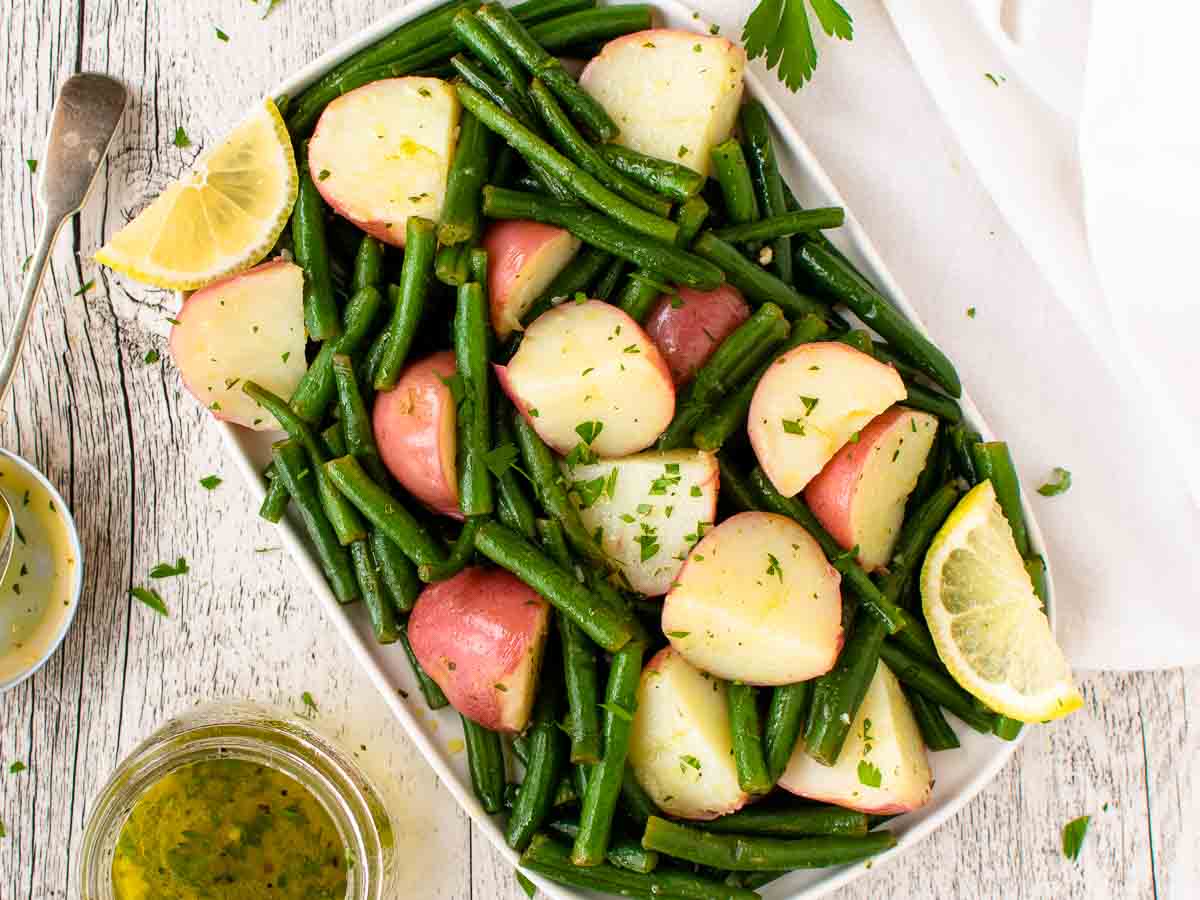 Overhead view of potatoes and green beans on a white oblong plate.