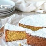 Spanish almond cake on a wooden board with a slice cut and slightly pulled out.