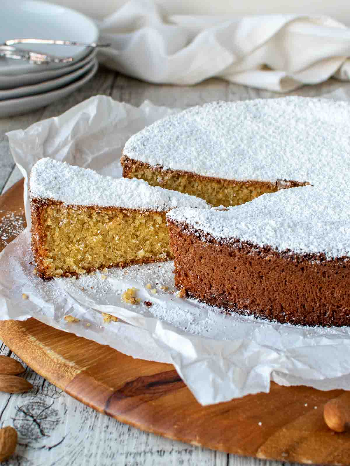 Spanish almond cake on a wooden board with a slice cut and slightly pulled out.