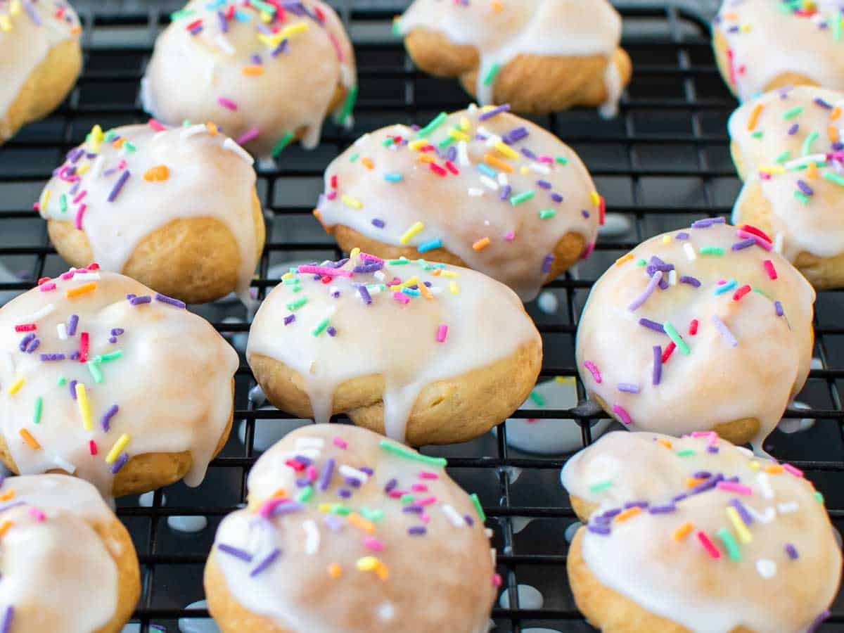 Cookies with white icing and rainbow sprinkles on a wire rack.