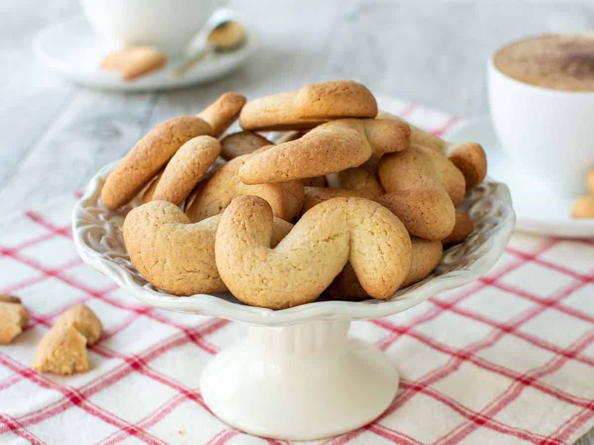 S shaped plain cookies on a white cake plate on a red checked cloth.