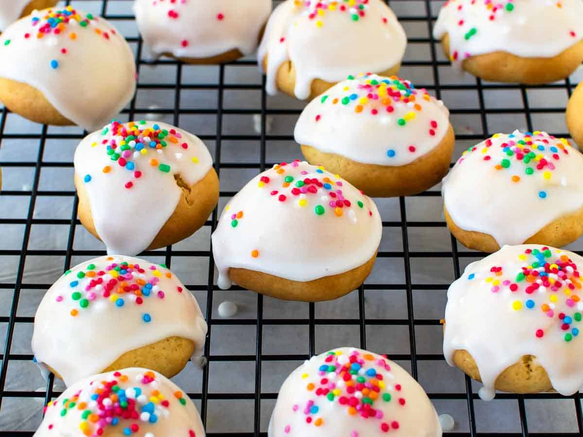 Close up of cookies with white icing and colored sprinkles on a wire cooling rack.
