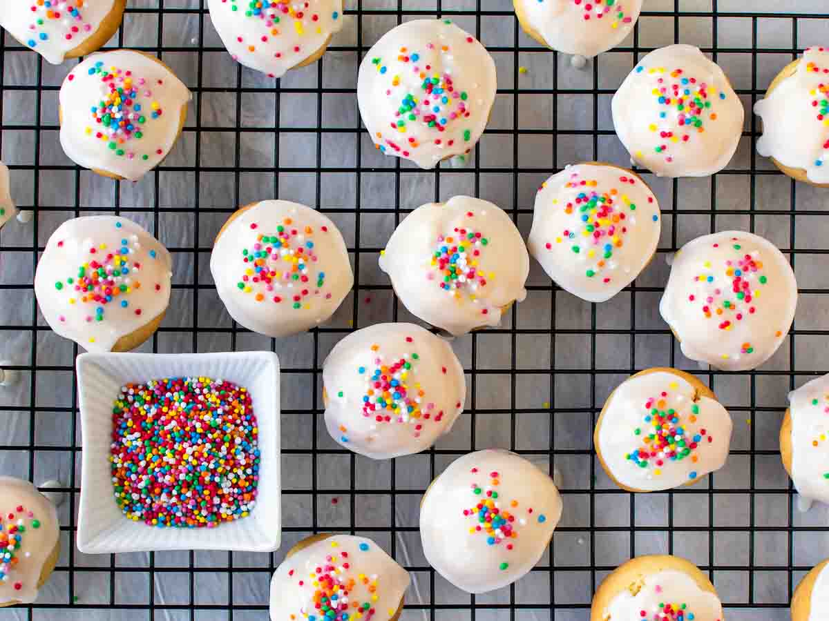 Overhead view of cookies with white icing and rainbow sprinkles on a black wire rack.