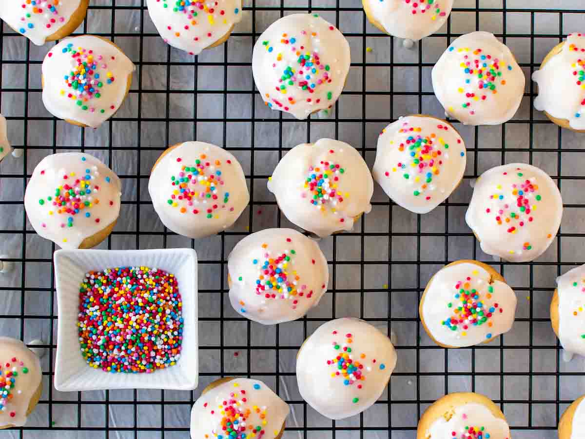 Overhead view of cookies with white icing and rainbow sprinkles on a black wire rack.