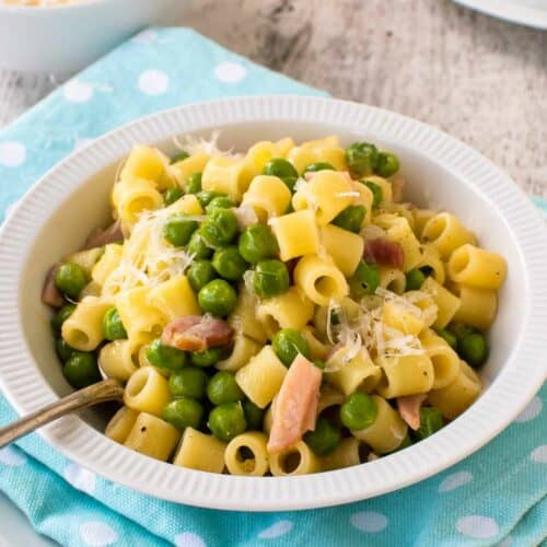 Pasta and peas in a white bowl on a sky blue napkin.