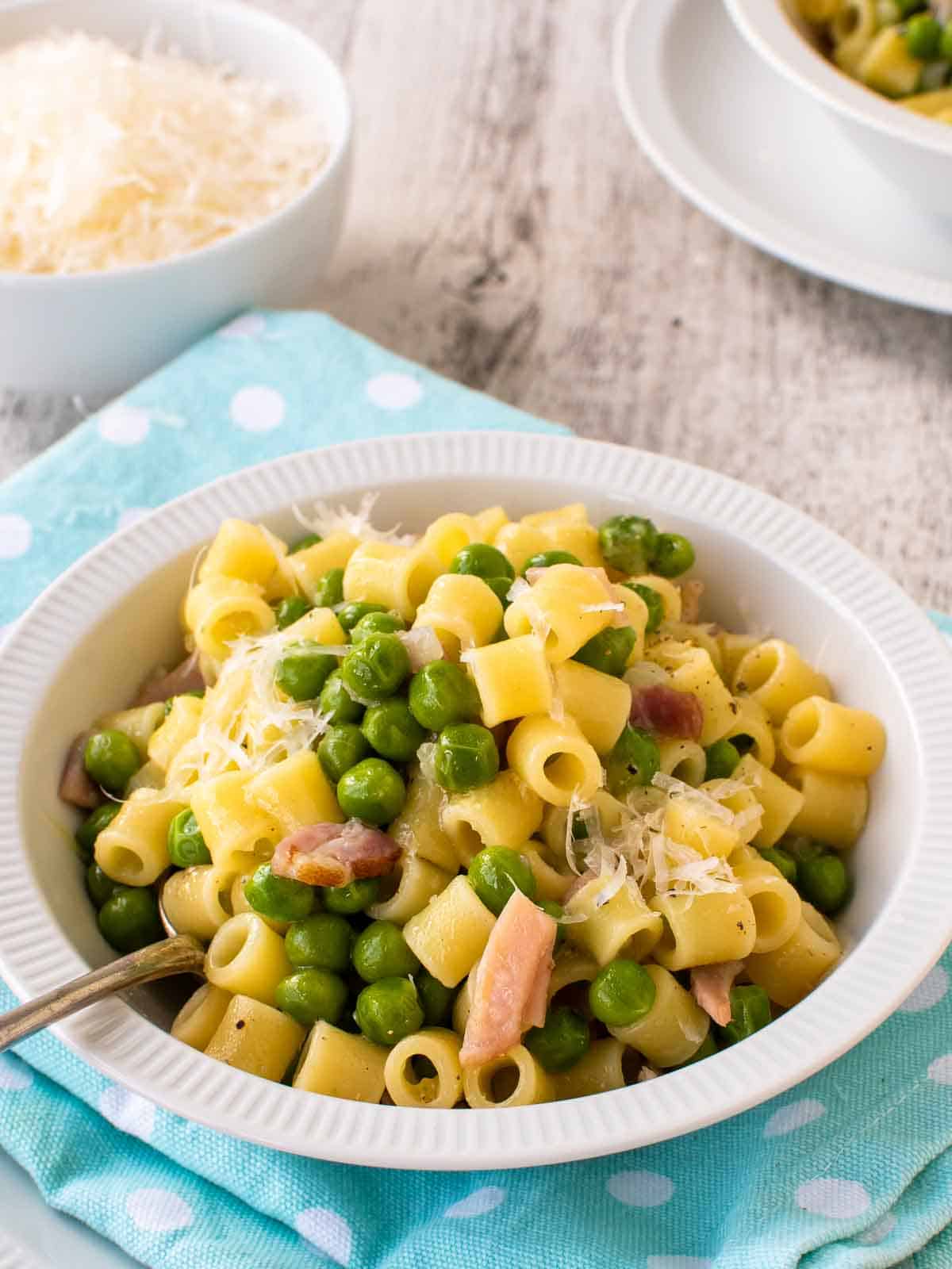 Pasta and peas in a white bowl on a sky blue napkin.
