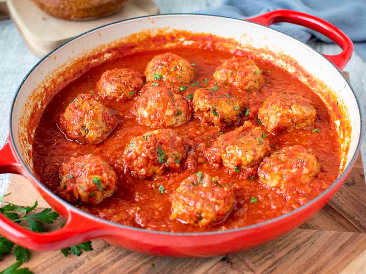 Meatballs in marinara sauce in a pan with red handles.