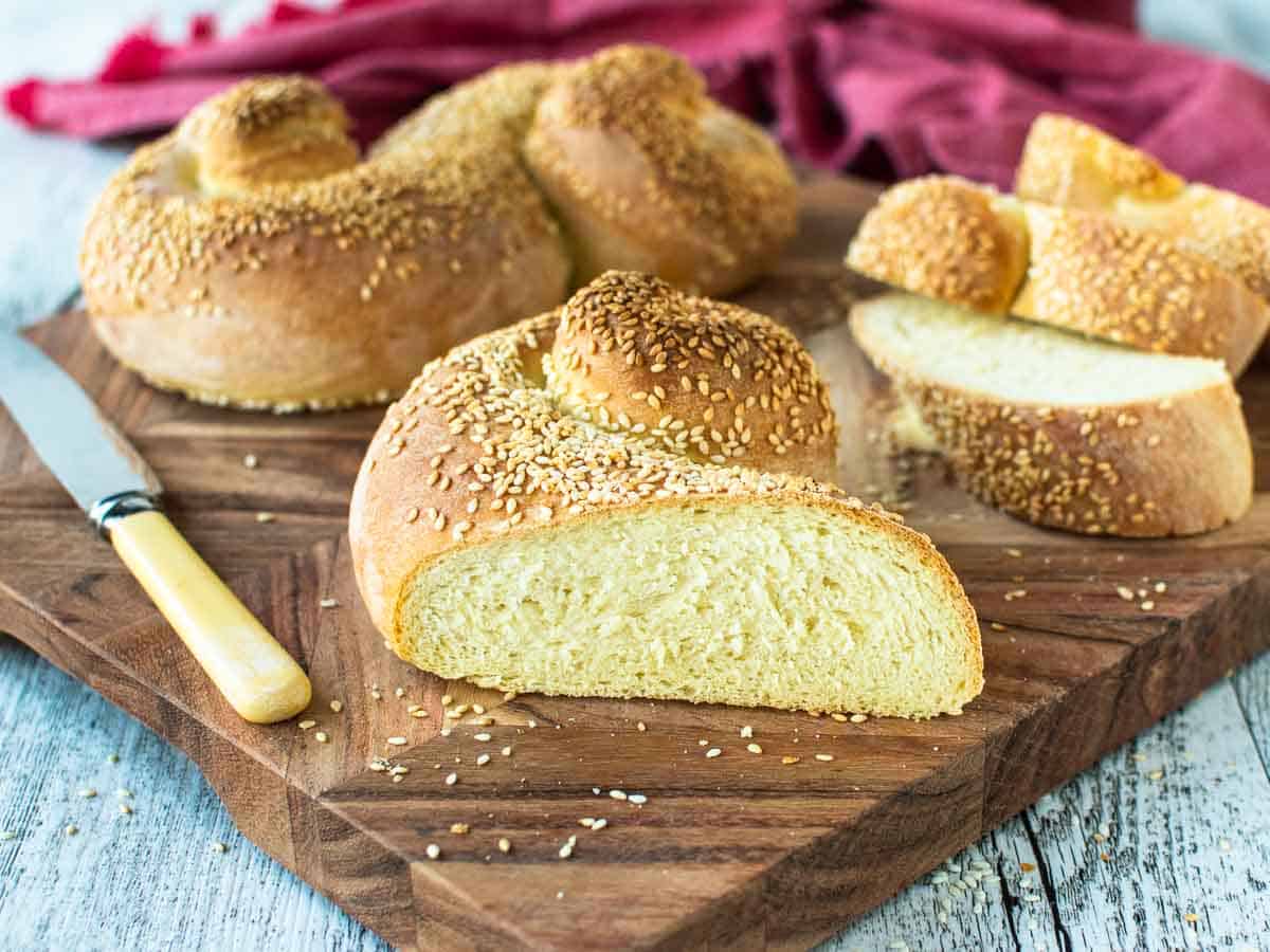 Bread topped with sesame seeds cut in half on a wooden board.