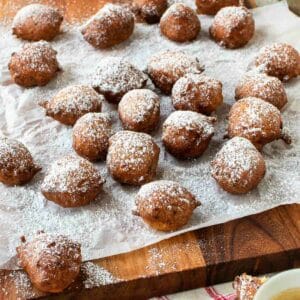 Fried sfingi dusted with powdered sugar scattered on a paper cover board.