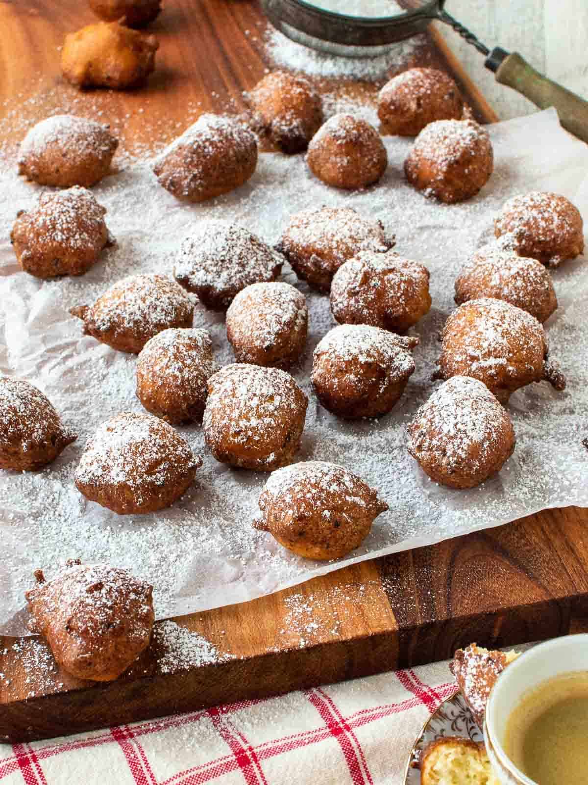 Fried sfingi dusted with powdered sugar scattered on a paper cover board.