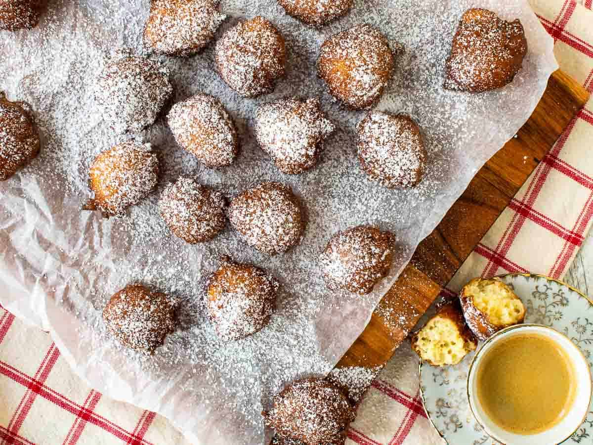 Overhead view of browned donut balls dusted with powdered sugar on a white paper covered board.