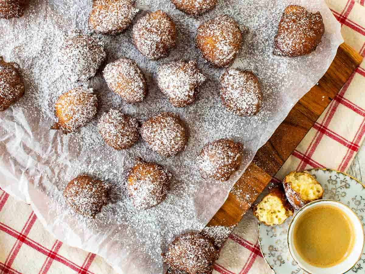 Overhead view of browned donut balls dusted with powdered sugar on a white paper covered board.