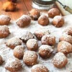 Fried sfingi dusted with powdered sugar scattered on a paper cover board.