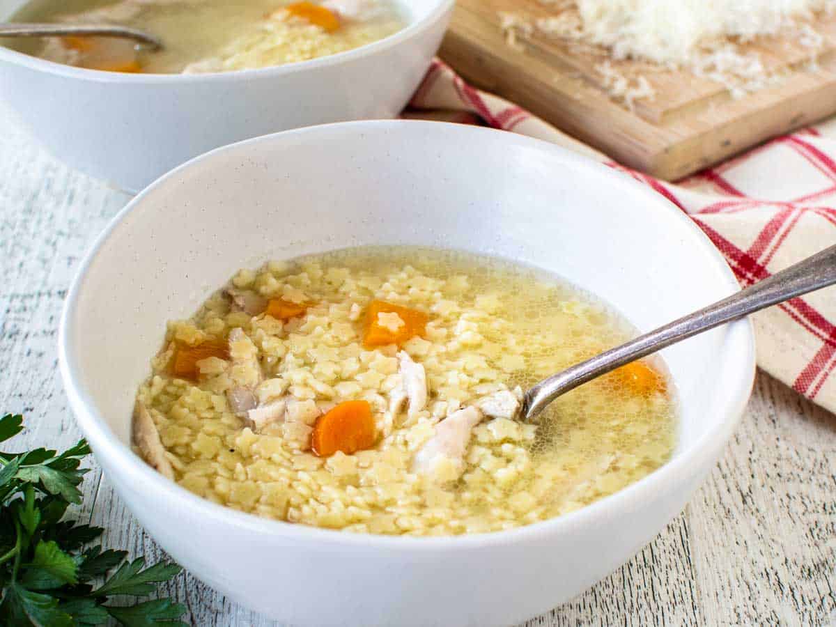 White bowl filled with chicken and pasta broth.