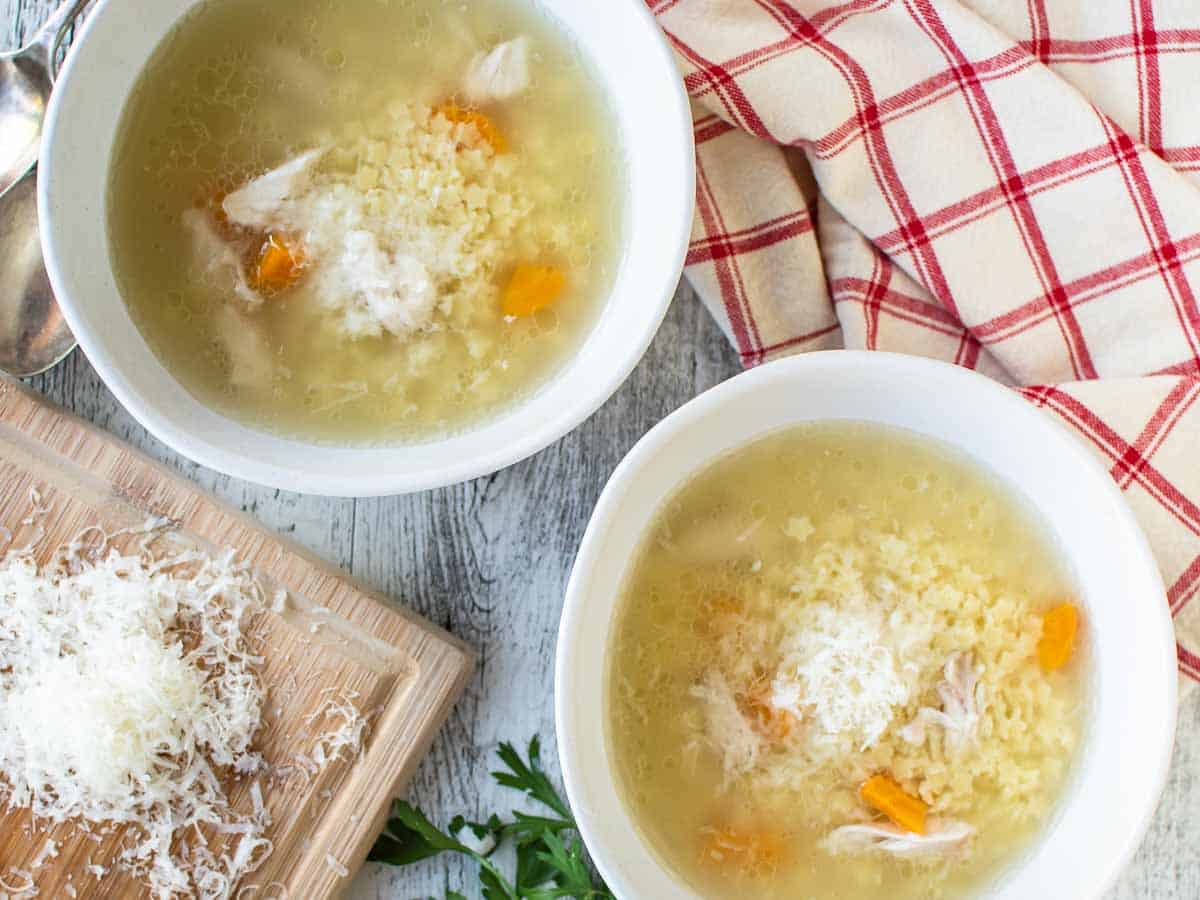 Overhead view of two white bowls filled with chicken and small pasta soup.