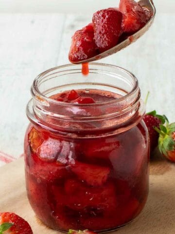 Strawberry Compote in a glass jar with a spoonful being poured in.