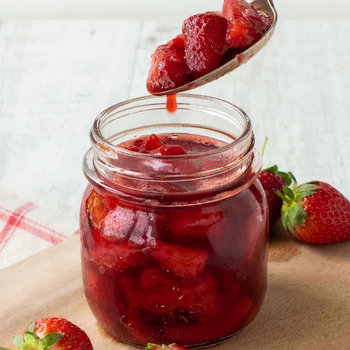 Strawberry Compote in a glass jar with a spoonful being poured in.