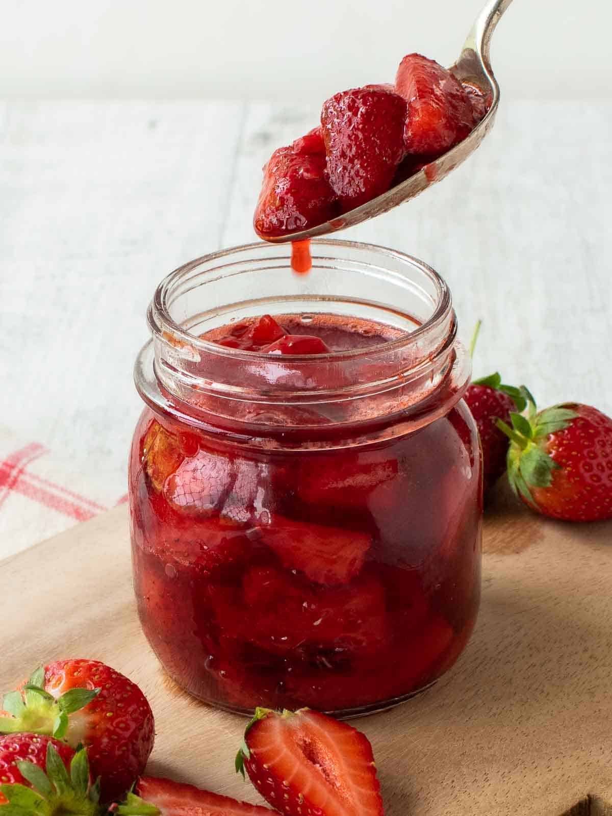 Strawberry Compote in a glass jar with a spoonful being poured in.