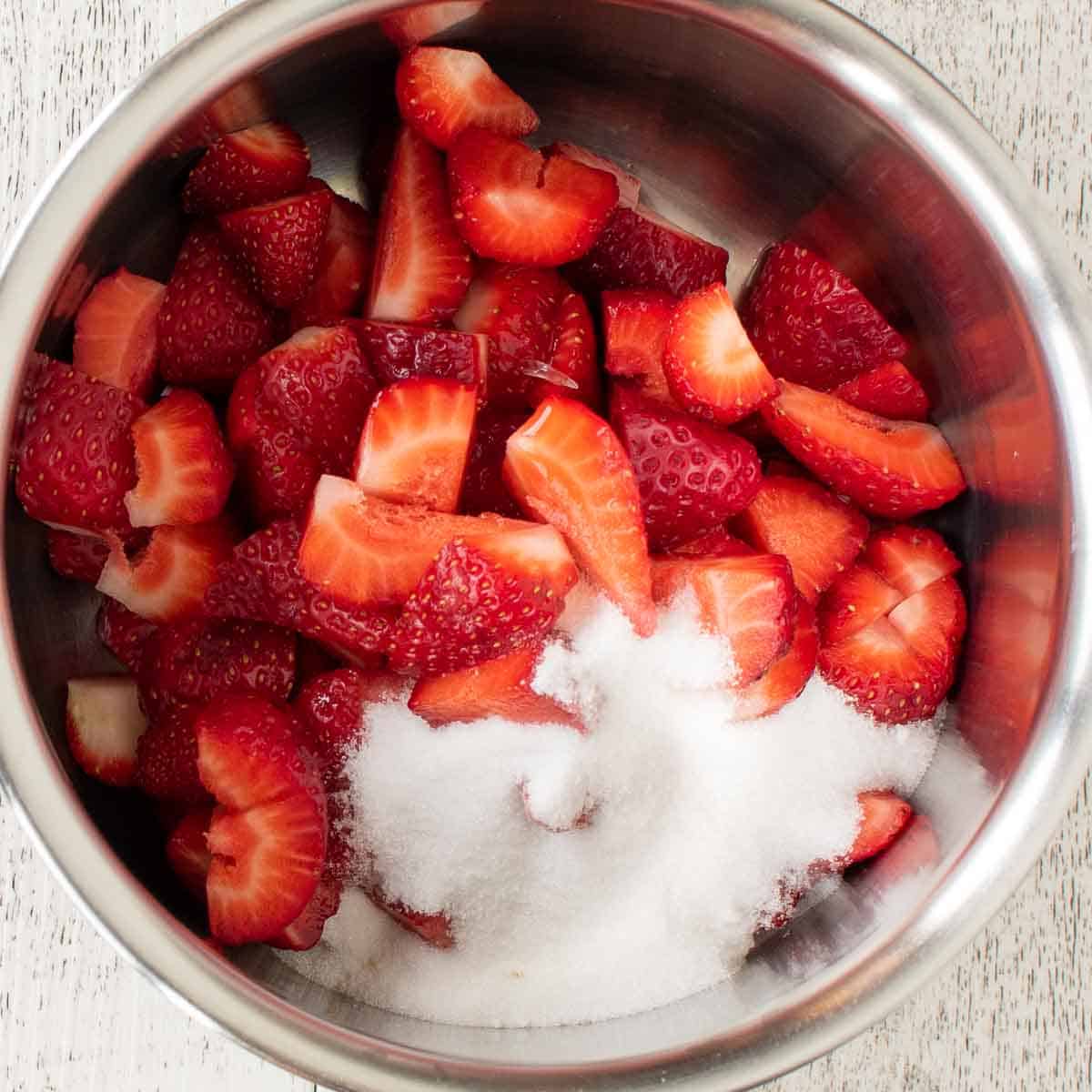 Cut up strawberries and white sugar in a saucepan viewed from above.