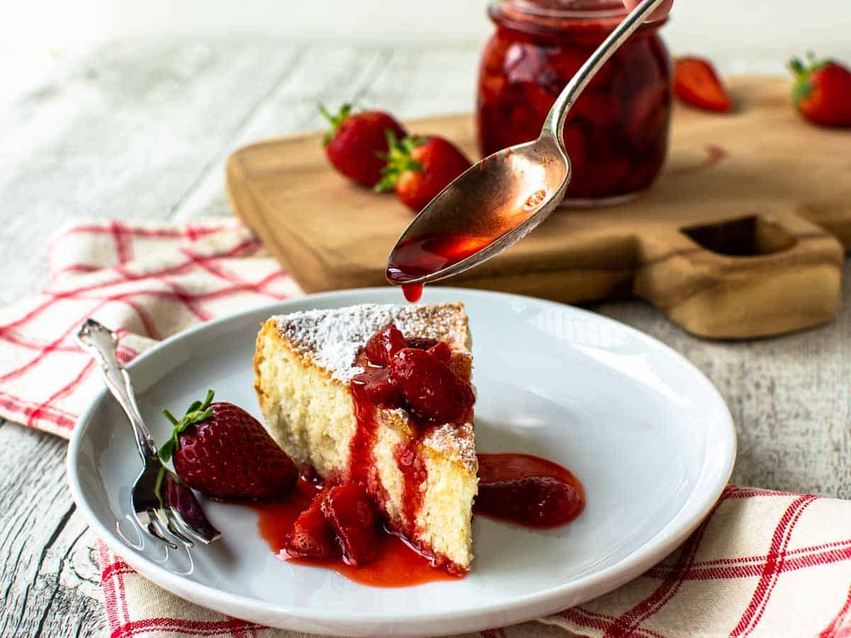 Wedge of yellow cake with chunky strawberry sauce being poured over it.